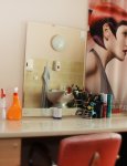 Pomieszczenie fryzjera. Toaletka fryzjerska z lustrem. Obok lustra na ścianie plakat z modną fryzurą kobiecą